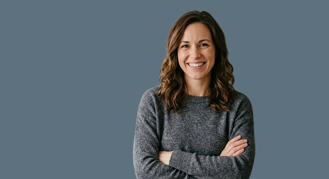 Confident middle-aged woman with arms crossed smiling at camera on gray background