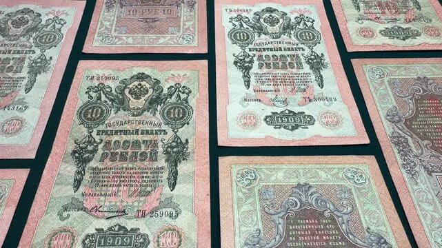 Collection of antique 10 ruble banknotes from 1909 Russian Empire arranged on a soft pink background, showing detailed patterns, faded colors and historic paper money for finance.