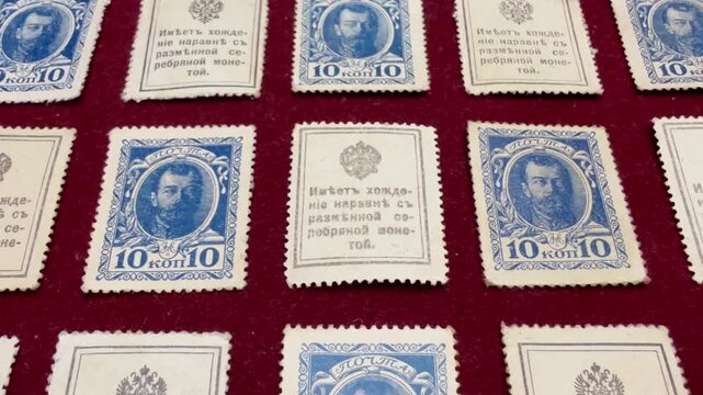 Close-up of vintage blue and cream 10 kopeck of 1915 Nicholas II Russian Empire postage stamps arranged on red fabric, showing portrait designs and old printed text, ideal for history, collecting.