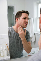 Fototapeta premium Man examines skin condition in mirror at home bathroom during daytime afternoon