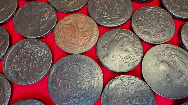 Close view of assorted old 2 kopeck coins 1757-1762 Russian Empire Elizabeth I spread on bright red fabric, showing worn metal surfaces, engraved details, and a vintage money collection background.