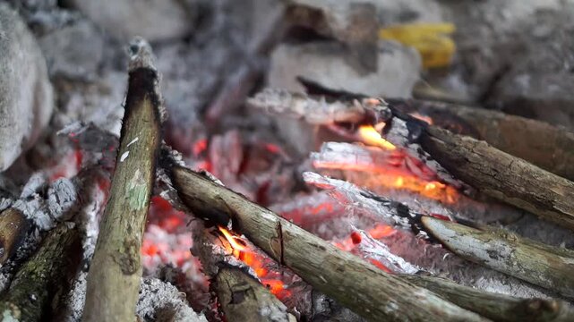 Close-up shot of bright orange flames burning traditional firewood inside a simple outdoor stone hearth.	