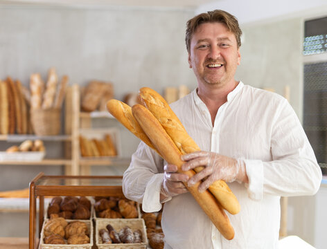 Man customer holding loaf of bread and baguettes with hands in disposable gloves.