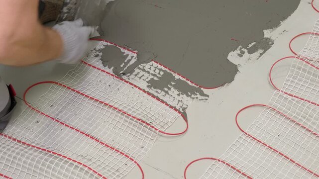 Electric Heating Mat Installing in the Tile Adhesive. Underfloor Dual Core Fiberglass Mesh Mat. Warm Floor Heating System. Warming. Worker Applying Concrete Mortar for Warm Floor. Renovation work. 4K