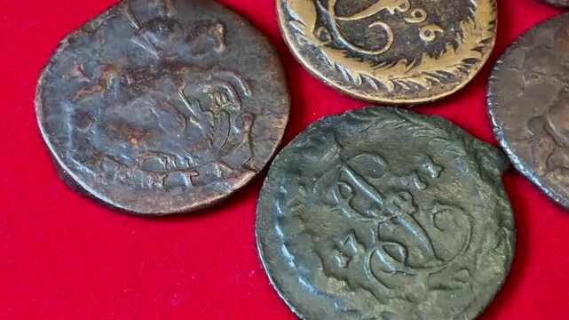 Close view of several old worn Denga coins 1764-1796 Russian Empire Catherine II on bright red fabric, showing aged metal texture, engraved marks, and a vintage collection feel.