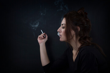 Young woman smoking cigarette exhaling smoke in profile view against dark background © Catsense