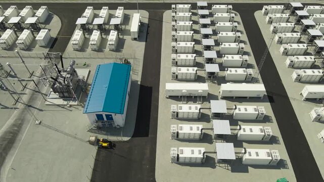 Drone footage capturing a modern Battery Energy Storage System, or BESS, featuring rows of high capacity industrial containers and an electrical substation for renewable power grid stability