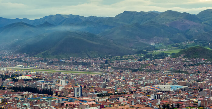 Cusco, Cuzco, Peru, Per&uacute;: Panoramic cityscape with Alejandro Velasco Astete airport, urban stadium and illuminated neighborhoods beneath vast Andean mountains at dusk.