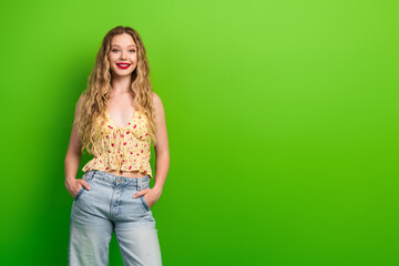 Obraz premium Glamorous young woman with blonde hair posing in floral top and jeans against a vivid green background