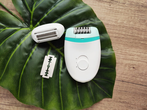 Electric epilator with a detachable head and razor blade placed on a large green leaf. Body care, hair removal, feminine hygiene and beauty concept. Top view.