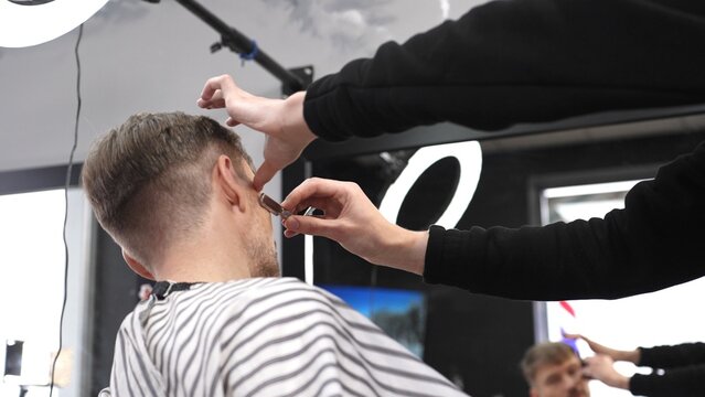 Skilled barber performing precise hair fade using straight razor, working on client's hair in contemporary grooming salon with professional tools