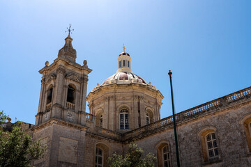 Fototapeta premium old medieval church Maltese building with bell tower and detailed limestone brick building with clear blue summer skies overhead on sunny day