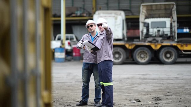 Experienced supervisor and younger logistics coordinator verify shipment records and inspect cargo information at a container terminal. Documentation review and operational monitoring.