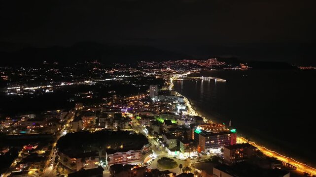 Aerial night skyline over beachside town soft warm lights, curved bay, calm water reflections, distant