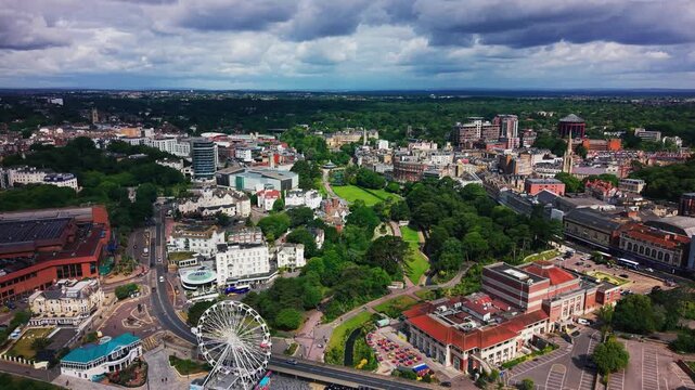 Aerial drone footage of Bournemouth town centre showing the urban skyline, Lower Gardens, roads, hotels, historic buildings, modern developments and a large observation wheel under dramatic