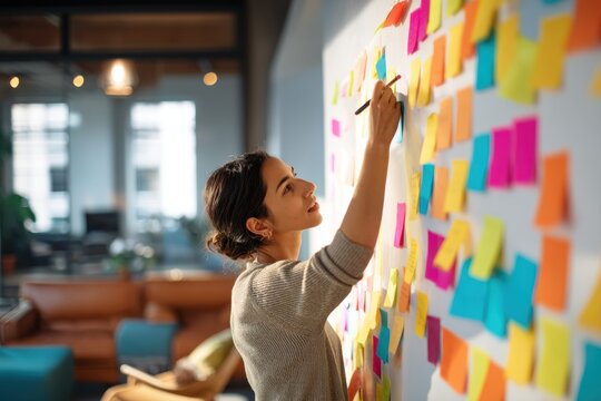 Woman manager writing on sticky notes attached to glass wall. Creative professional brainstorming project strategy in office. Idea development, planning, startup management and productivity.