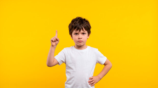 Young boy with serious expression points finger up against a vibrant yellow background