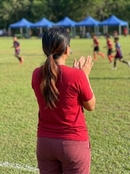Soccer fan clapping for youth players on green field in sharp rear view for sports community marketing