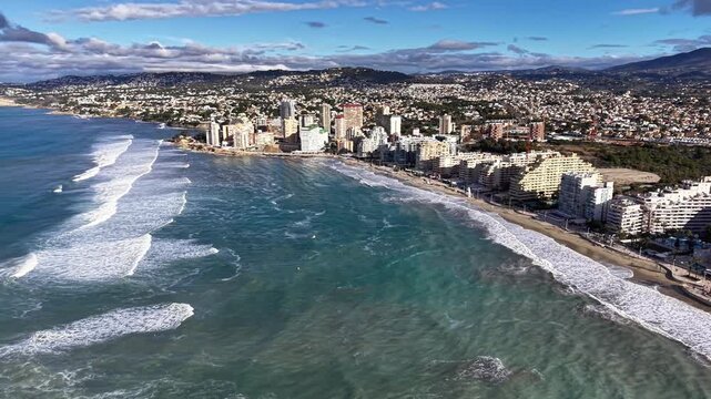 Expansive oceanfront city panorama with surf, wide breakers and swells, sweeping shoreline curves, busy