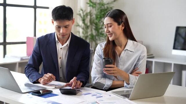 Asian colleagues discussing financial data and business strategy during a collaborative meeting in a modern office, using a calculator and analyzing documents