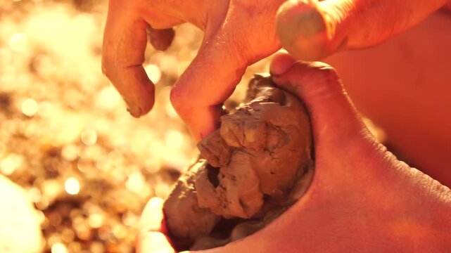 Hands clay shaping, close-up of dirty hands molding wet mud on a sunny day outdoors, creativity