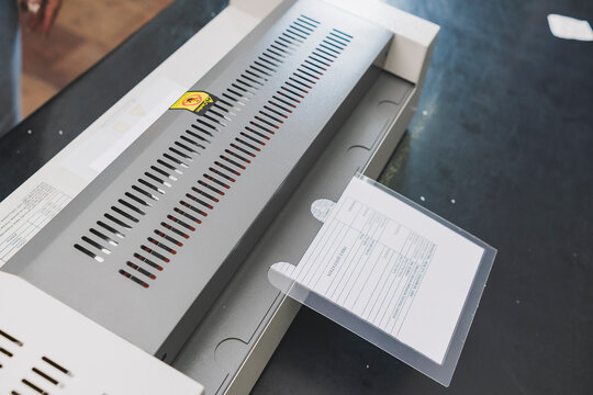Document inside laminating machine with transparent pouch film, creating protected and durable printed materials for office use and storage.