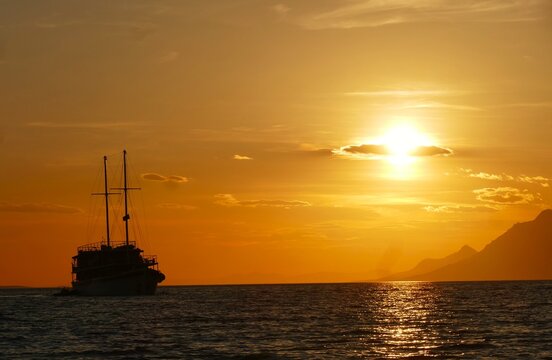 Big touristic boat silhouette on the sea in orange sunset with clouds and magical horizon