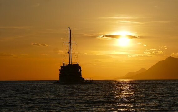 Big touristic boat silhouette on the sea in orange sunset with clouds and magical horizon