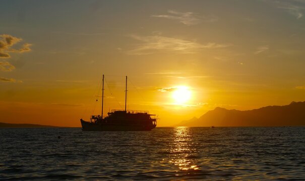 Big touristic boat silhouette on the sea in orange sunset with clouds and magical horizon