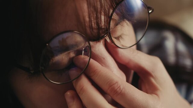 Close-up portrait of tired woman adjusting eyeglasses and rubbing eyes. Female experiencing eye strain, fatigue, stress or headache while working indoors. Vision problems, exhaustion and health