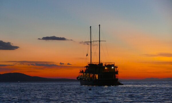 Big touristic boat silhouette on the sea in orange sunset with clouds and magical horizon