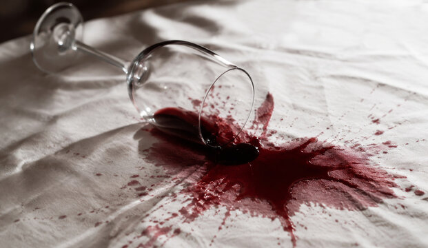 Red wine spilled from overturned glass on white tablecloth. Wine stain on fabric background. Accident with alcohol at dinner party. Risk of damage to textile and home cleaning concept.