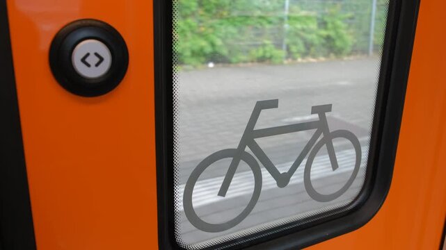 Bicycle icon sign on orange door window of moving passenger train with button