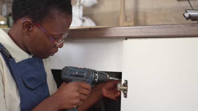 Black female carpenter using a power drill to install a cabinet hinge