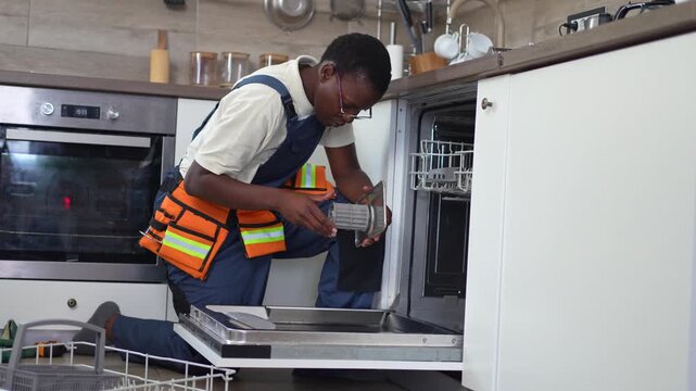 African-American repairman repairing a dishwasher in a kitchen
