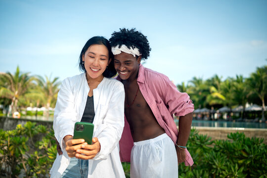 Diverse couple connected, embracing technology and social media while enjoying moments at the beach