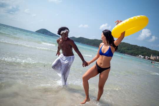 Happy couple running on a sandy beach with inflatable rings during a tropical vacation