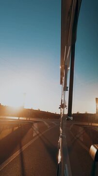 Side view of a bus driving on a highway through the countryside during a beautiful golden sunset, passing under a bridge with the sun creating a strong lens flare and long shadows