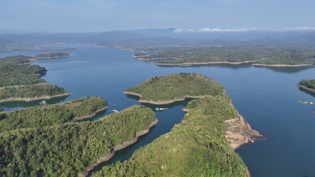 Drone footage captured over Ta Dung Lake in Dak Nong Province, Vietnam, at sunrise. The drone gradually descends toward the lake, documenting calm waters, forested islands, and the surrounding highlan