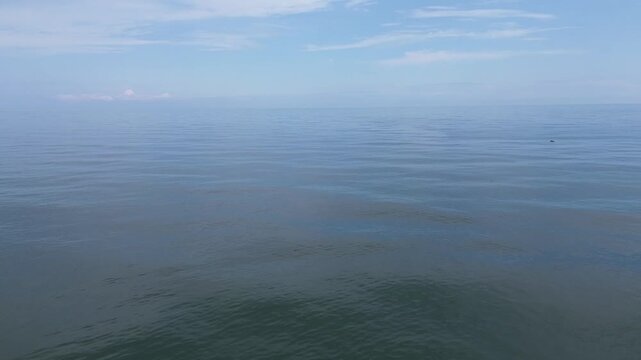 Smooth aerial drone footage flying forward at low altitude over the open Black Sea near Batumi, Georgia. The shot captures waves, the hazy horizon, and a blue cloudy sky. Raw, unedited footage with na