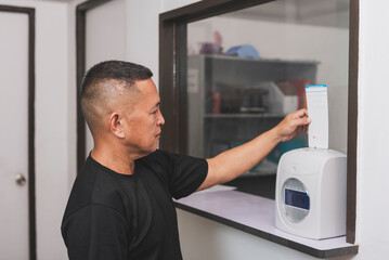 Obraz premium A middle-aged office worker inserts attendance card into a time recorder machine to clock in for work, tracking employee hours and workplace attendance.