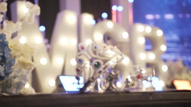 The queen and king's crowns at the prom night look elegant against a luxurious, brightly lit stage backdrop.