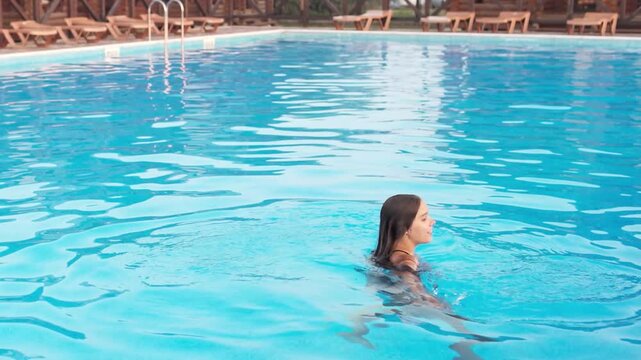 Girl in leopard swimsuit playing in the pool under the summer sun