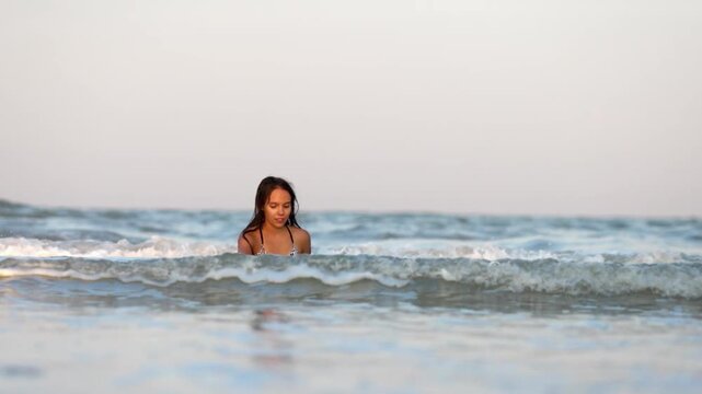Girl with wet hair in a leopard swimsuit splashes water while sitting in the sea