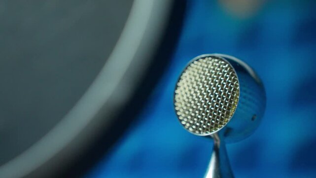 Round metallic microphone centered right with blue blurred background, stable setup evolving