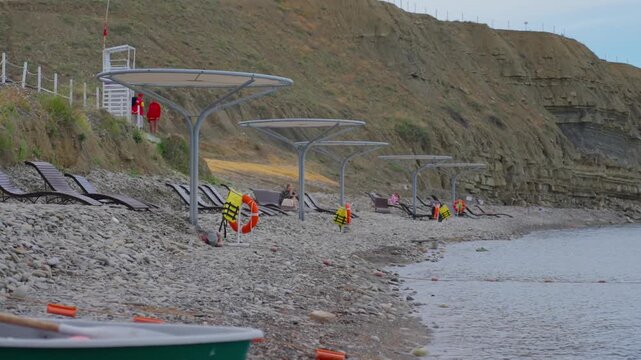 Lifeguards monitoring pebble shore with row of sunshades and loungers under overcast light