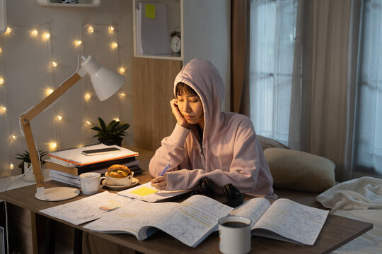 Young woman was stressed and tired while doing homework in Home Workspace under warm desk lamp, snacks and coffee