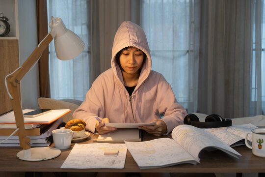 Focused young woman Reviewing Lessons in Under Workspace Warm Desk Lighting Late Night with Snacks and coffee