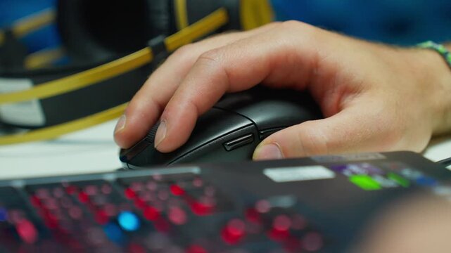Gamer hand controlling mouse over RGB keyboard with headphones in background at late sequence