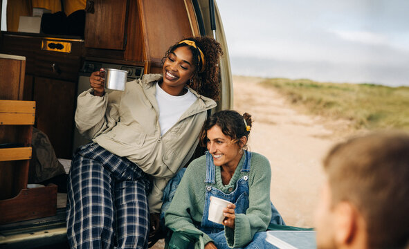 Friends enjoy coffee and conversation at the back of a camper van
